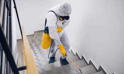 Pest Control exterminator, in work gear spraying pesticide in a stairway.